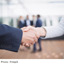 Poignée de main entre deux travailleurs en habit sur fond de travailleurs discutant
